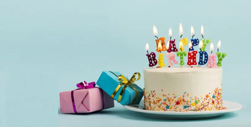 Birthday cake with lit letter candles beside wrapped gifts on a blue background