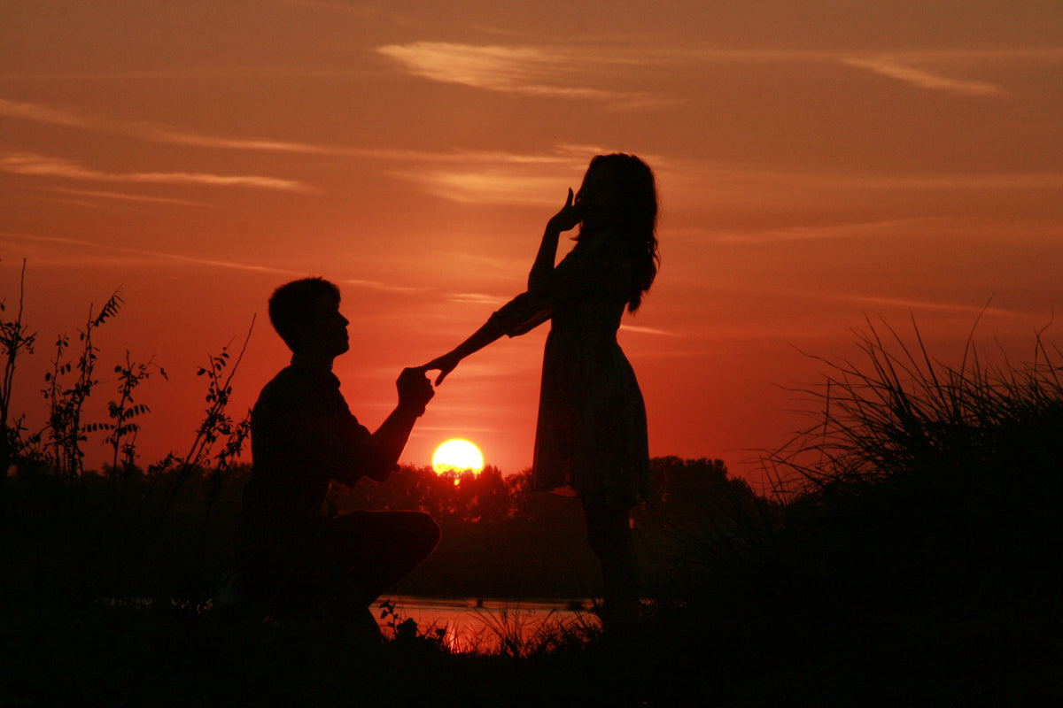 Silhouette of a person kneeling to propose to a partner at sunset