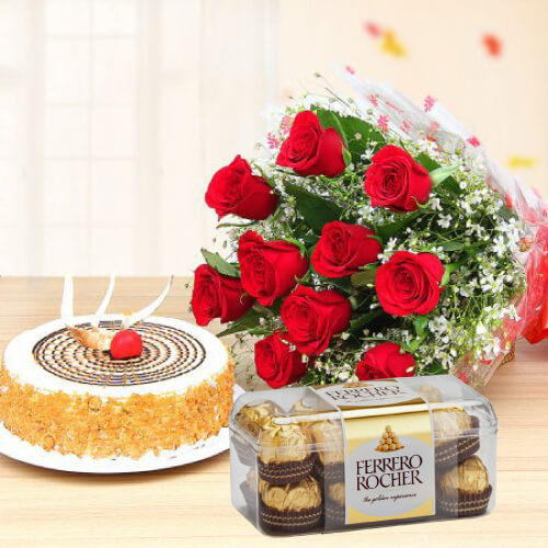 A combination of a round cake with chocolate pieces on top, a bouquet of red roses, and a box of Ferrero Rocher chocolates presented together.