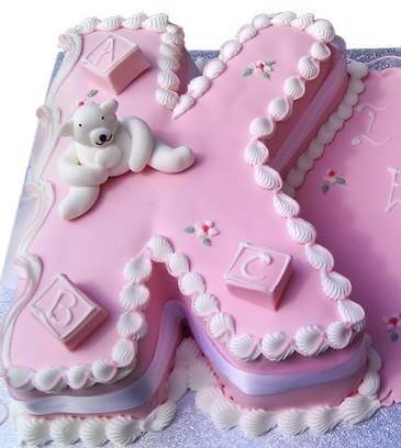 Pink Letter K Cake — a pink K with baby-themed decorations and pale edging; India