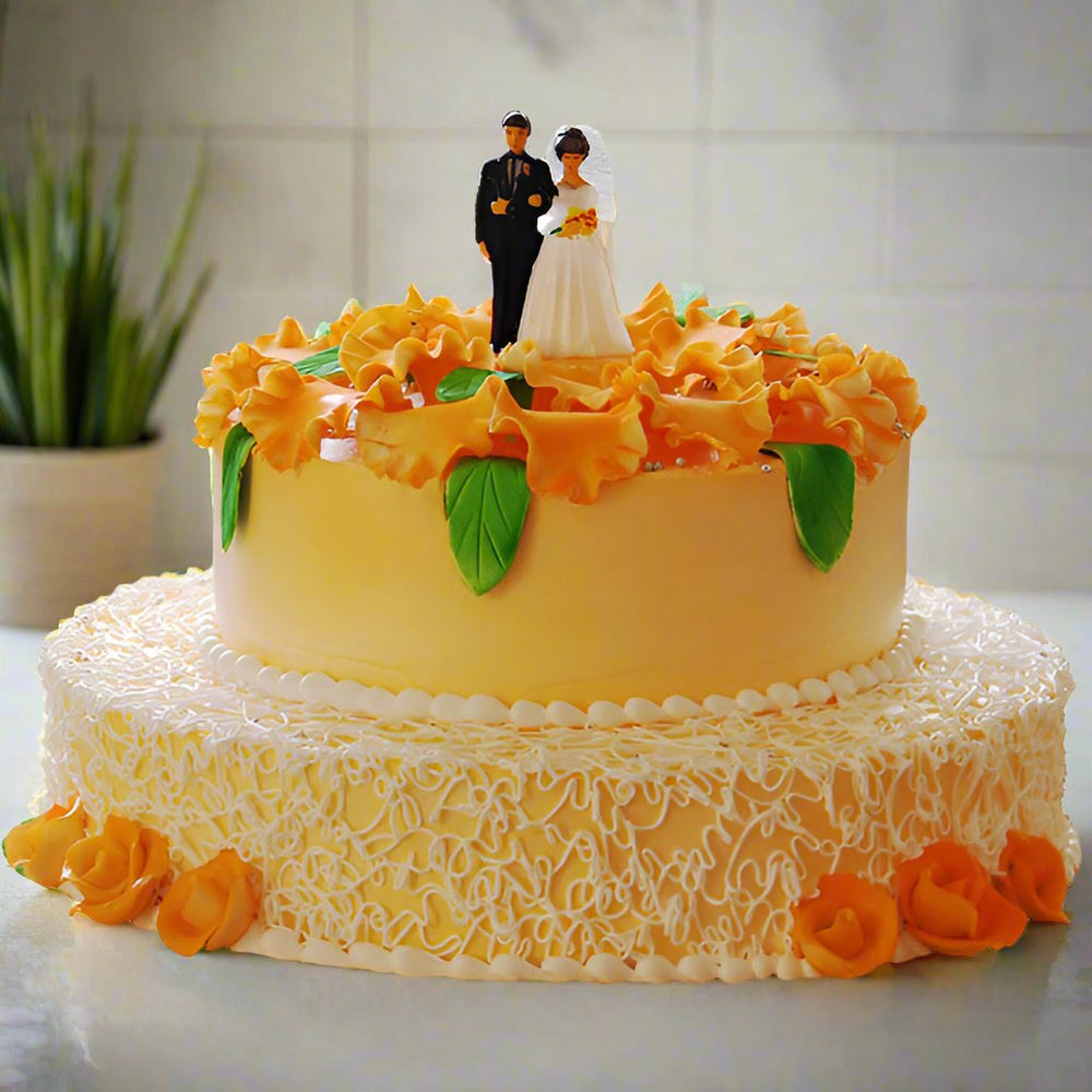 Wedding Cake — pale wedding finish, orange flowers and a couple topper; India