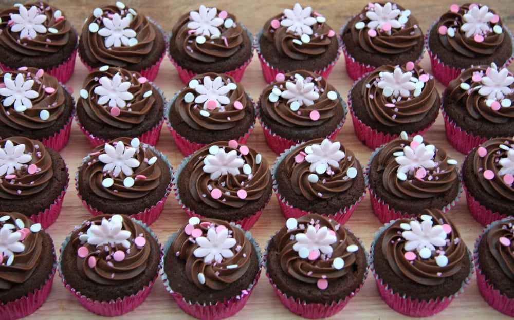Flower Design Chocolate Cupcakes 24 Piece — dark frosting with small pale flowers and sprinkle accents; India