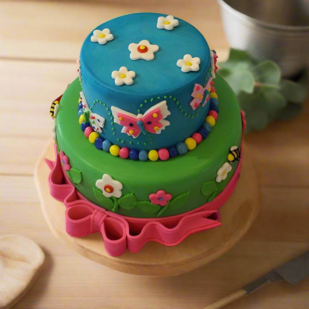 Fondant Birthday Cake — blue-and-green tiers, colourful stars and a pink bow border; India